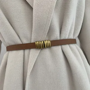 Primo piano di sottile cintura in pelle marrone con fibbia in ottone sul cappotto.