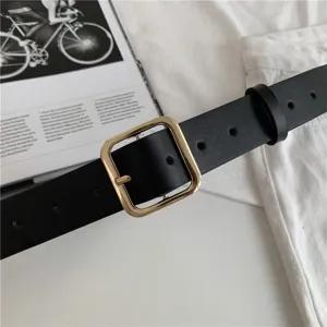 Close-up detail of a classic black leather belt featuring a sleek metallic gold square buckle.