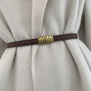 Primo piano di una sottile cintura in pelle marrone chic con fibbia metallica dorata sul cappotto.
