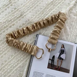 Dettaglio cintura elastica dorata, con design arricciato e raffinata fibbia in metallo.