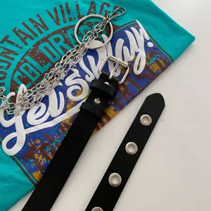 Close-up detail of punk style black waist belt with metal grommets and silver chains.