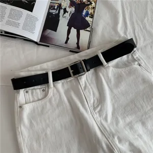Classic black leather belt with silver square metal buckle, detailed view on white jeans.