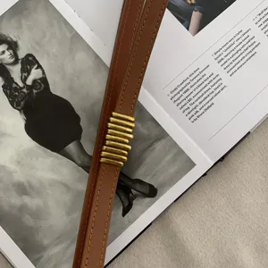 Primo piano di una sottile cintura in pelle marrone da donna con fibbia metallica dorata.