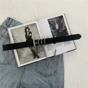Detail view of punk style black leather belt with metal rings and chain on flat lay fashion setup.
