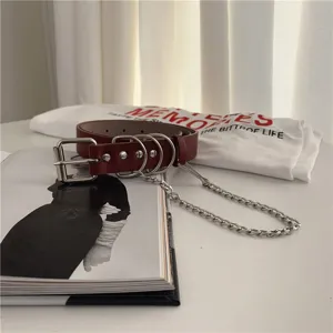 Close-up detail of dark red punk leather belt featuring multi metal rings and silver chain accessory.