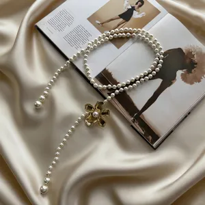 Gros plan d'une élégante chaîne de taille en perles avec pendentif fleur dorée.