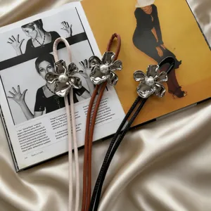 Close-up detail shot of stylish thin leather cord belt featuring metal flower and pearl buckle.