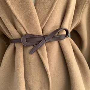 Gros plan d'une élégante ceinture nœud en similicuir marron foncé sur un manteau chameau.