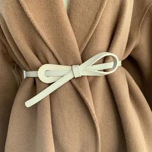 Vue rapprochée détaillée d'une ceinture nœud en cuir beige minimaliste sur manteau en laine.