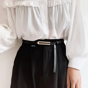 Dettaglio in primo piano della sottile cintura in pelle da donna con fibbia elegante su pantaloni.