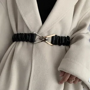 Detail shot of a black elastic waist belt featuring a stylish metallic triangular buckle.