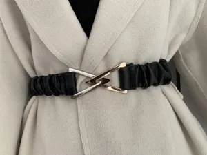 Elegant black stretch dress belt detail featuring metallic interlocking triangle buckle.