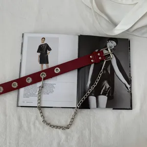 Detailed view of red punk style leather belt with metal eyelets, grommets and hanging chain.