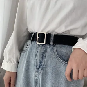 Detail shot of a black leather belt featuring a sleek silver square buckle worn on denim.