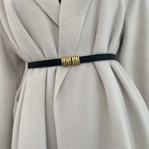 Dettaglio della sottile cintura nera in vita, fibbia dorata vintage, elegante accessorio per cappotto.