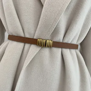 Dettaglio in primo piano di una sottile cintura in pelle marrone su un cappotto beige.