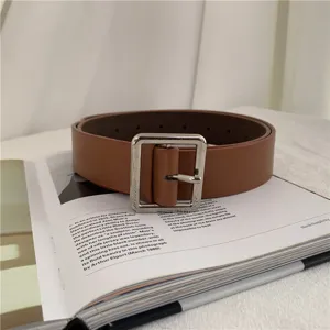 Detail shot of a stylish brown leather belt with a square silver metal buckle placed on a book.
