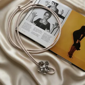 Detailed shot of a chic beige soft leather rope belt featuring a metallic flower and pearl pendant.