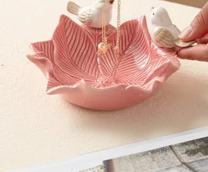 Close-up of ceramic pink leaf jewelry dish featuring cute little birds for neat storage.