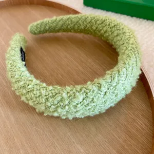 Primo piano dettagliato di un cerchietto intrecciato in tessuto bouclé verde, morbido.