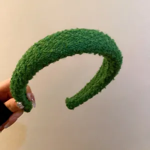 Primo piano della fascia per capelli intrecciata in peluche verde, con tessuto texturizzato.