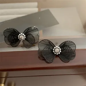 Gros plan de boucles d'oreilles papillon creuses noires avec perles et strass délicats.