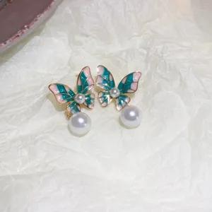 Close-up detail of stylish green and pink butterfly pearl earrings with sparkling diamond accents.