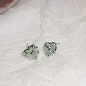 Detailed view of irregular green heart stud earrings with silver border and sparkling crystal.