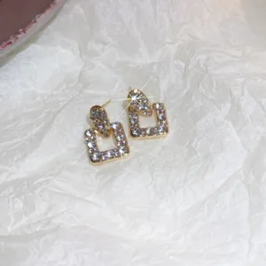 Detailed close-up shot of elegant gold-toned square geometric earrings sparkling with stones.