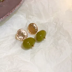 Elegant green resin drop earrings with gold hammered disc detail on textured white background.