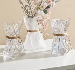 Nahaufnahme nordischer Origami-Glasvasen mit Juteband und Blumenarrangement für Heimdekoration.