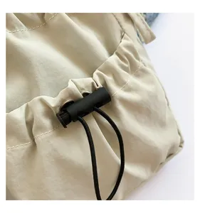 Detail view of beige nylon drawstring bag pocket with black cord lock and adjustable pull string.