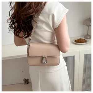 Detail shot of a stylish minimalist beige shoulder bag with a metal buckle worn by model.