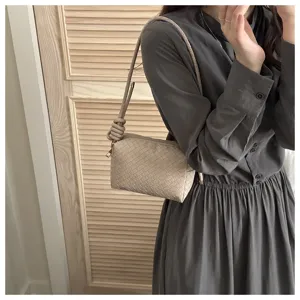 Beige woven leather shoulder bag detail, stylish knotted strap and compact camera shape.
