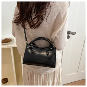 Detailed shot of a stylish black glossy leather crossbody bag worn on back, daily outfit.