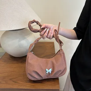 Detailed close-up of brown textured underarm bag with cute silver butterfly and ruched strap.