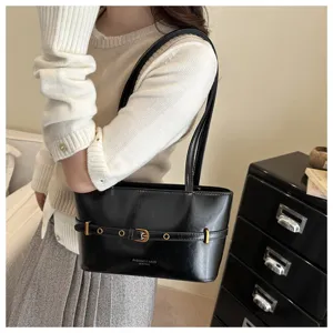 Close up detail of black patent leather shoulder bag with stylish metal belt buckle design.