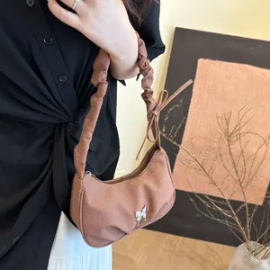 Detail shot of a brown ruched underarm bag featuring a delicate metal butterfly accessory.