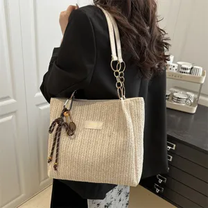 Detail view of stylish beige woven straw tote bag with chain strap and cute decorative pendant.