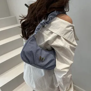 Detail shot of the pleated denim shoulder bag with chic metal butterfly ornament on back.