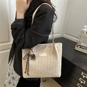 Detail view of woven straw tote bag with ribbon charm and chain strap for summer style.