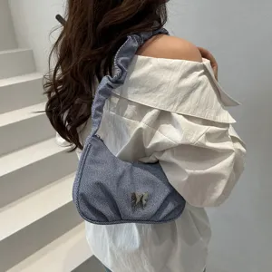 Detail shot of blue denim shoulder bag, ruched strap design and cute metal butterfly accent.