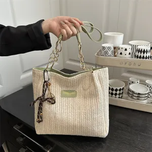 Woven straw shoulder tote bag with green leather strap and metal chain detail for women.