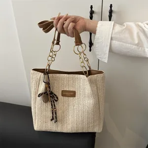 Vista detallada de un elegante bolso de paja tejido con asas de cadena y detalles.