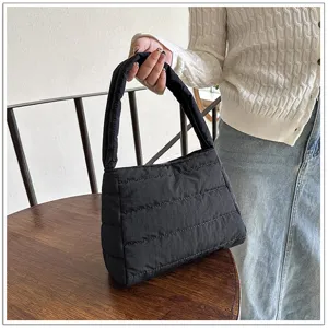 Detail shot of a black nylon quilted shoulder bag held by a model over a rustic wooden table.