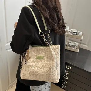 Woven straw tote bag detail showing green leather straps, metal chain, and beach style look.