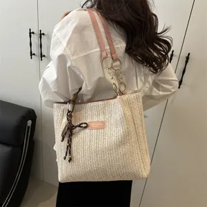 Detail view of the stylish woven straw tote bag with pink leather straps and chic chain accent.