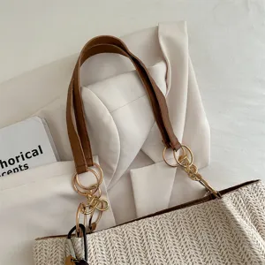 Woven straw tote bag detail with brown leather handles and gold metal ring chain links.