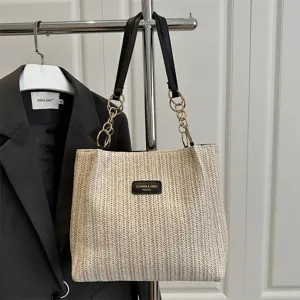 Detail view of casual woven straw tote bag with black leather straps and stylish chain design.
