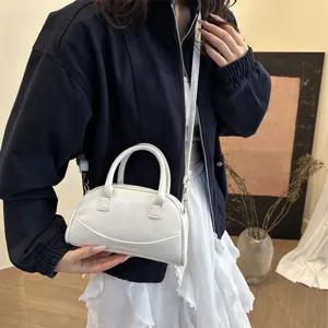 Detailed view of a sleek white mini Boston bag featuring dual top handles and a crossbody strap.